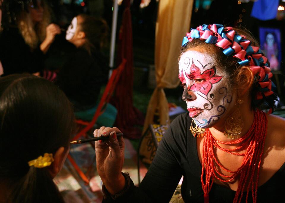 A woman paints a girl's face for Dia de los Muertos.