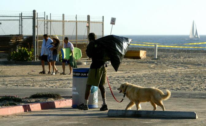 A homeless man with his dog stops at a trash bin to search for recyclable cans as beach-goers head home for the day at Venice Beach in Los Angeles, California, 28 August 2003.