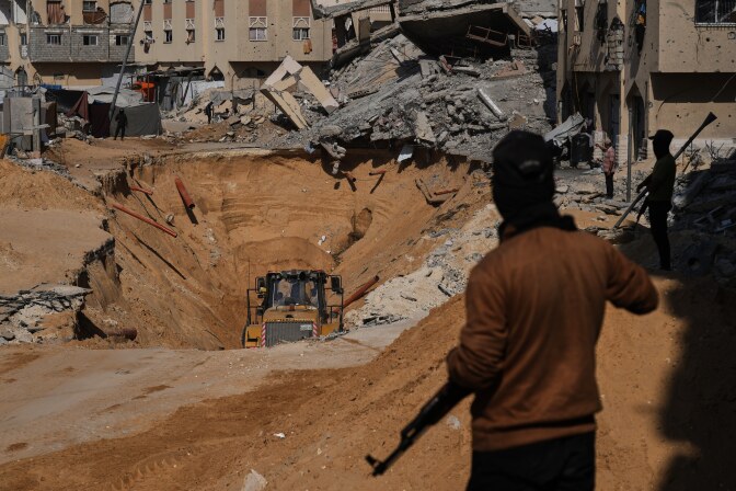 Men with weapons stand near a large hole in the ground.
