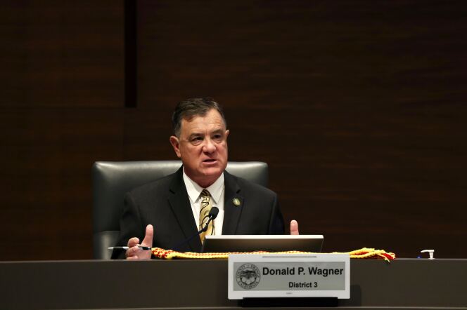 A white man in a dark suit speaks into a microphone while gesturing with his hands.