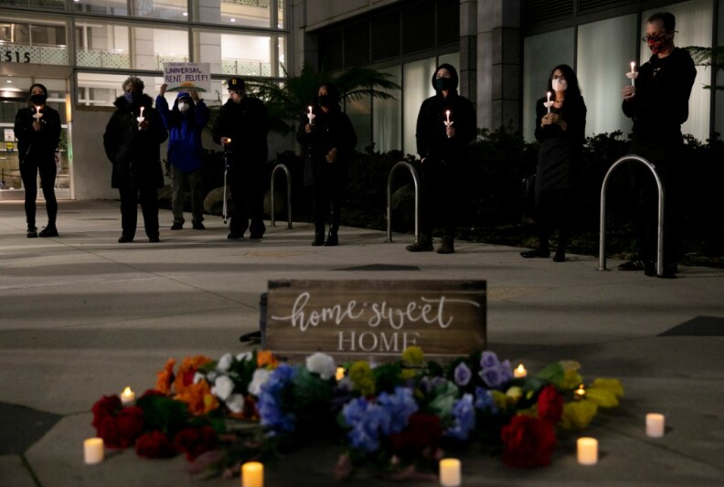 Protesters carry lighted taper candles near a sign that reads: "Home Sweet Home" and is surrounded flowers and lighted votives.
