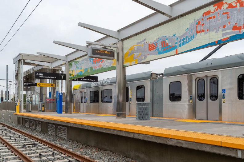 A train waits at a station platform with a large mural visible on the walls behind it.