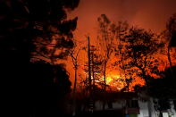 The yellow, orange, and red glow from a fire behind a home and trees at night 