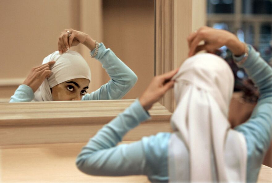 A woman adjusts her hijab, a head covering worn by female observant Muslims.