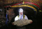 A man in a white full-body suit, headlamp and gloves stands in the middle of a sewer holding a pale conglomerate that's about the size of a large toddler.  