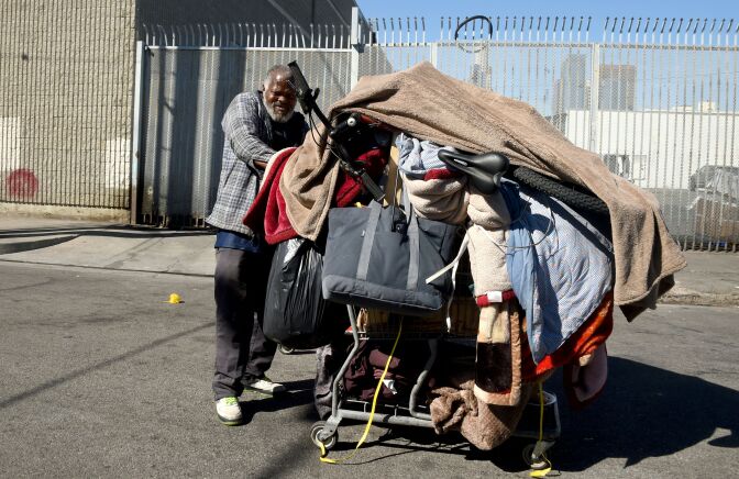 A homeless man pushes his cart of belongings along a street in Los Angeles, California on February 9, 2016.
