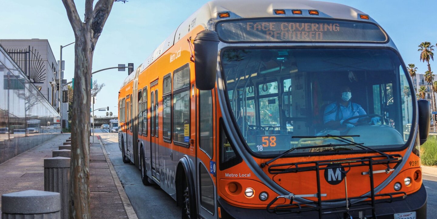 An orange Los Angeles Metro bus drives along a street.