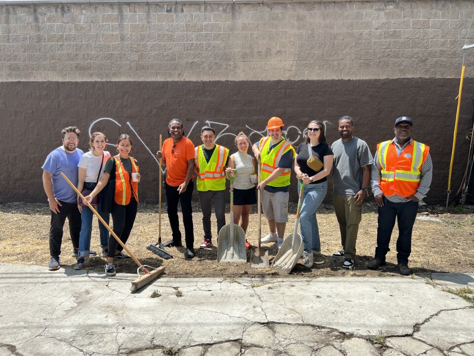 A row of smiling volunteers, some dressed in orange and neon green vests and holding shovels and brooms. 