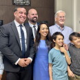 A group of adults and children smile together outside a courtroom door labeled Superior Court Department W13.