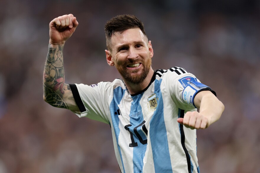 A man in a light blue and white vertical striped jersey riause his right arm and smiles.