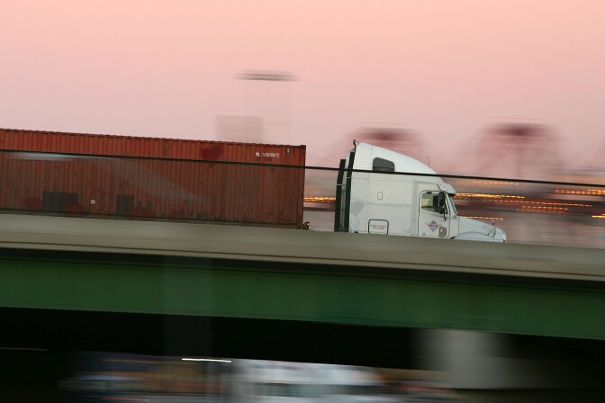 LONG BEACH, CA - JULY 06:  A truck carries a shipping container at the ports of Long Beach and Los Angeles on July 6, 2006 in Long Beach, California. In the Los Angeles area, studies indicate that diesel exhaust from trucks, locomotives, heavy equipment and ships causes cancer and is responsible for 70% of pollution-related health problems and hundreds of deaths every year. Rather than wait for the international agency that regulates the global shipping industry, the International Maritime Organization, to implement considered changes to strengthen emissions standards for cargo vessels, the ports recently unveiled an ambitious clean-air plan that could significantly improve air quality. The proposal seeks to reduce diesel emissions from cargo ships, trains and trucks by more than 50% over a five-year period at a cost of $2-billion.Almost 5,800 ships called at the ports of Los Angeles and Long Beach in 2005 released about 14,000 tons of air pollutants. Many ships emit as much exhaust per day as 12,000 cars.  (Photo by David McNew/Getty Images)