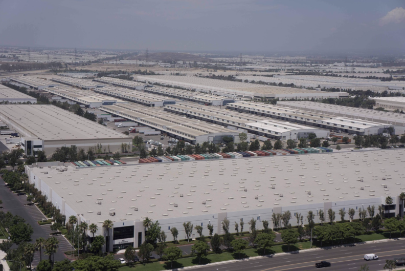 An aerial view of the roofs of vast grey warehouses, stretching far into the horizon
