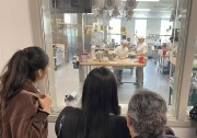 Three family members watch the student chefs work through a large window, where a cooking lab can be seen.