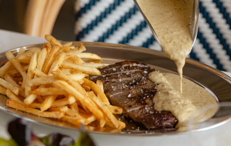 A gravy is poured on a silver platter of steak frites.