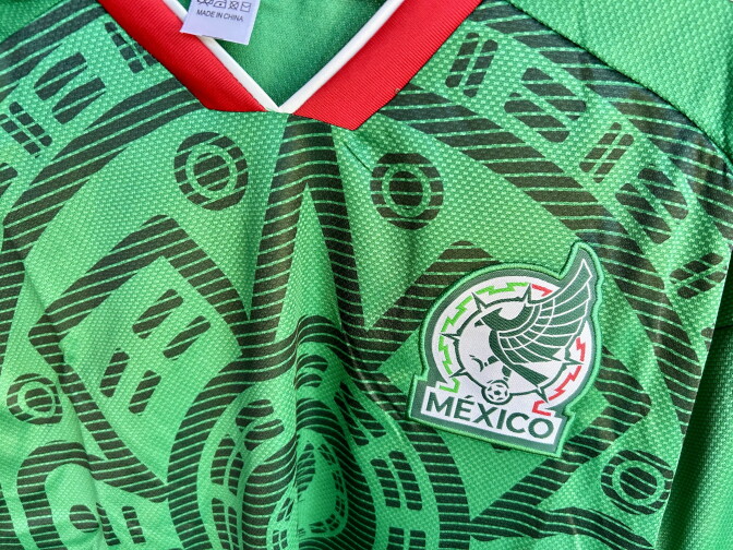 A greeen sports jersey with geometric designs and a logo with an eagle and the word, "Mexico".