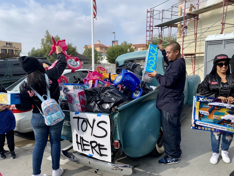 A handmade sign on the back of a low rider pick up truck reads: "Toys Here" People are filling the truck bed with toys.