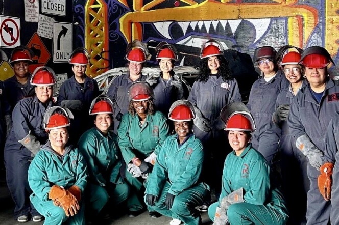 Female presenting people wear red constuction hats, gloves, and thick overalls.