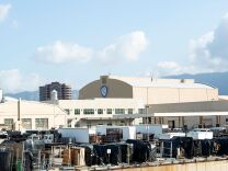 A wide view of several large beige warehouse-style buildings, one with the Warner Bros. logo. In front of the buildings are large trucks and movie equipment, mostly draped with black cloths. 