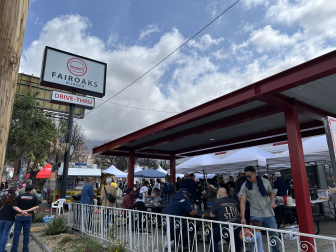 A crowd of people eat near a sign that reads FAIROAKS Burger Drive-thru