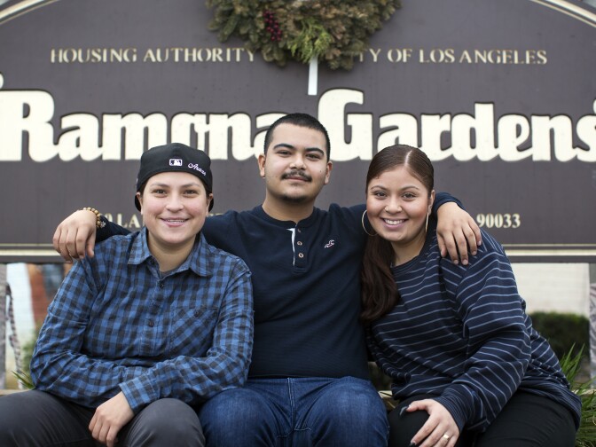 Ramona Gardens residents Marlene Arazo, left, Eddie Licon, and Amanda Gutierrez sit at an entrance to the public housing development in Boyle Heights on Friday, Jan. 13, 2017. The three grew up in Ramona Gardens in the 1990s being taught to keep their distance from the police.