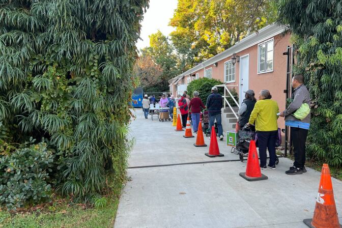 A line of people lining up along a driveway next to a peach color building.