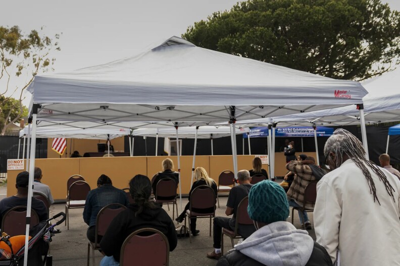 People sitting in chairs under a white canopy.