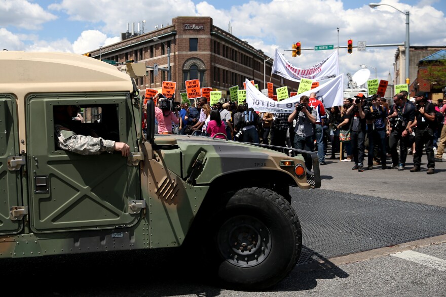 BALTIMORE, MD - MAY 02: A National Guard truck drives by protesters at North Ave., and Pennsylvania Ave., a day after Baltimore authorities released a report on the death of Freddie Gray on May 2, 2015 in Baltimore, Maryland. Marilyn Mosby, Baltimore City state's attorney, ruled the death of Freddie Gray a homicide and that criminal charges will be filed on six Baltimore City Police officers. Gray, 25, was arrested for possessing a switch blade knife April 12 outside the Gilmor Houses housing project on Baltimore's west side. According to his attorney, Gray died a week later in the hospital from a severe spinal cord injury he received while in police custody. (Photo by Patrick Smith/Getty Images)