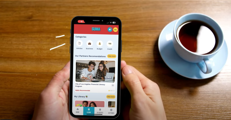 A cellphone is held with the screen showing a landing page for a finance app. A cup of coffee is placed beside the cellphone.