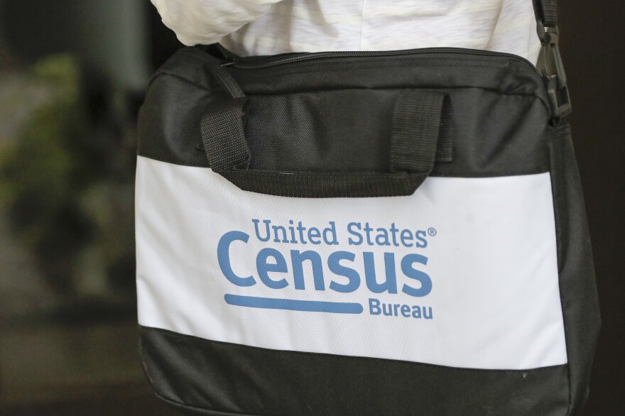 A person carries a messenger bag with a white label with blue lettering that reads "United States Census Bureau"