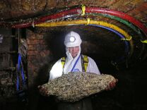 A man in a white full-body suit, headlamp and gloves stands in the middle of a sewer holding a pale conglomerate that's about the size of a large toddler.  