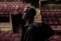 Side profile view of Andrew Scott standing in an auditorium. Red seats can be seen in the background.