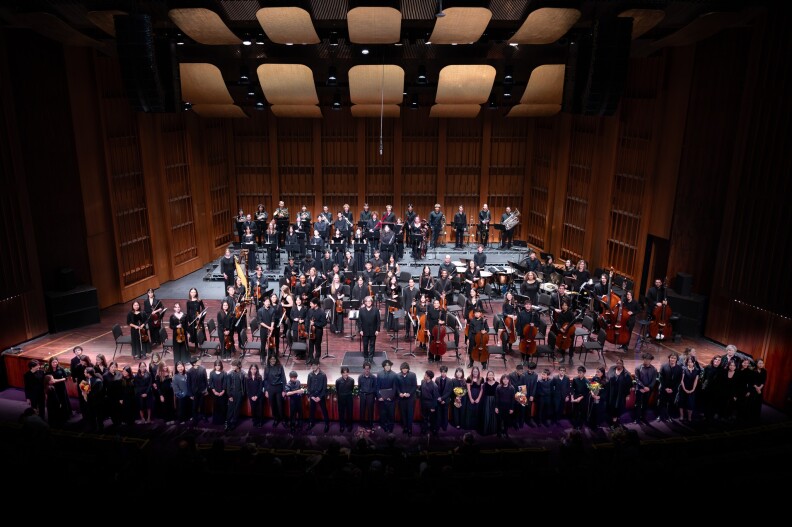 All members of the Los Angeles Youth Orchestra, dressed in black, stand facing the audience at the end of a performance.