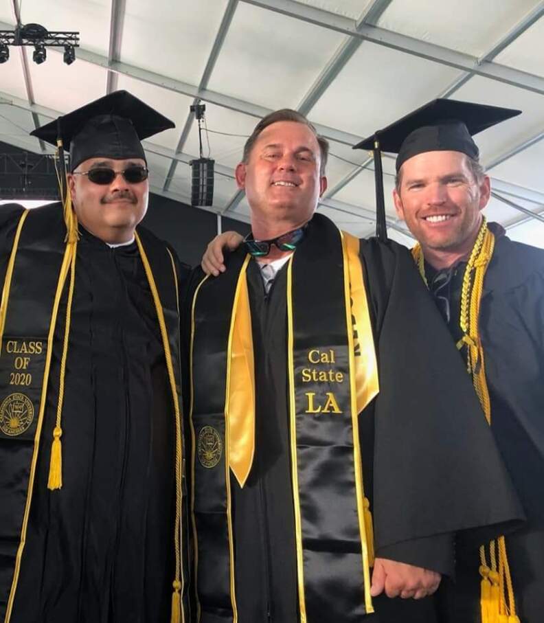 Three men wearing black graduation gowns smile and look into the camera. Their gowns read "Class of 2020" and "Cal State LA."