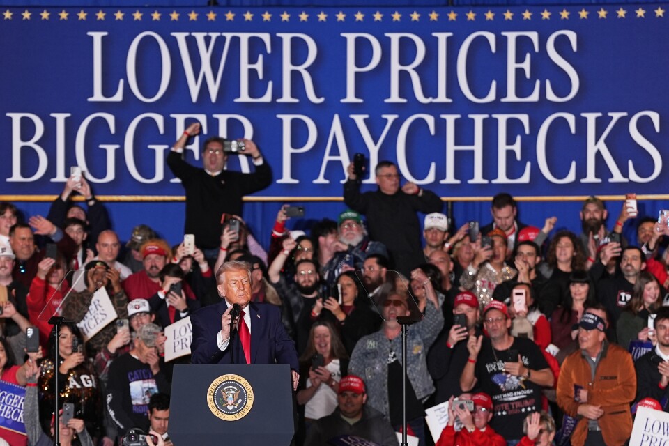 Donald Trump is at a lectern with seal of the President of the United States. Behind him and a group of people is a sign reading: Lower prices bigger paychecks.