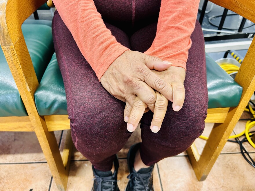 A person's hands with fingers interlaced on their lap.