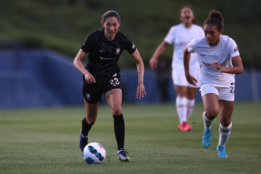 A soccer play moves the ball down the field while a defender chases after them.