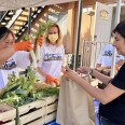 A female presenting person puts vegetables into a paper bag held by a female presenting person.