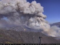 A large plume of smoke spreads over a mountain ridge.