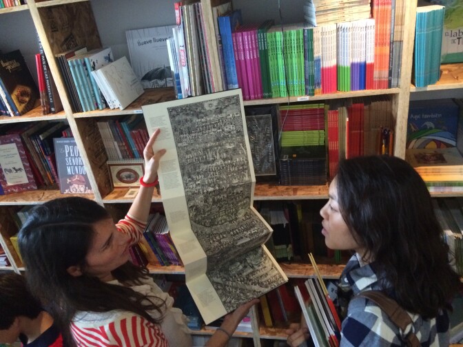 La Librería co-founder, Chiara Arroyo (left) shows a customer the children's book from Mexico called "Migrar," which open like an accordion and traces a family's migrant path from Oaxaca, Mexico to Los Angeles. 
