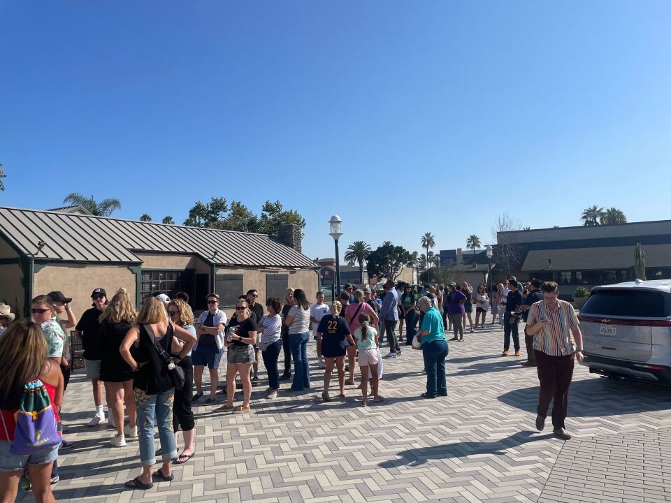 Dozens of people waiting in line outside in a plaza.
