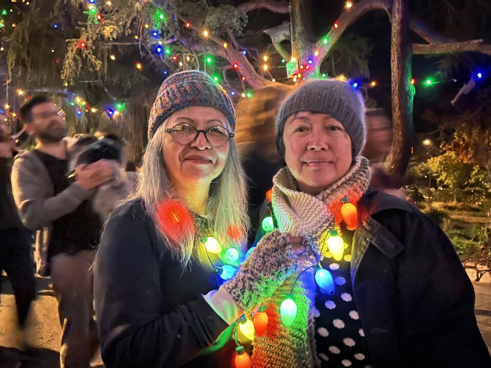 Two women wearing beanies are standing behind a festive scene
