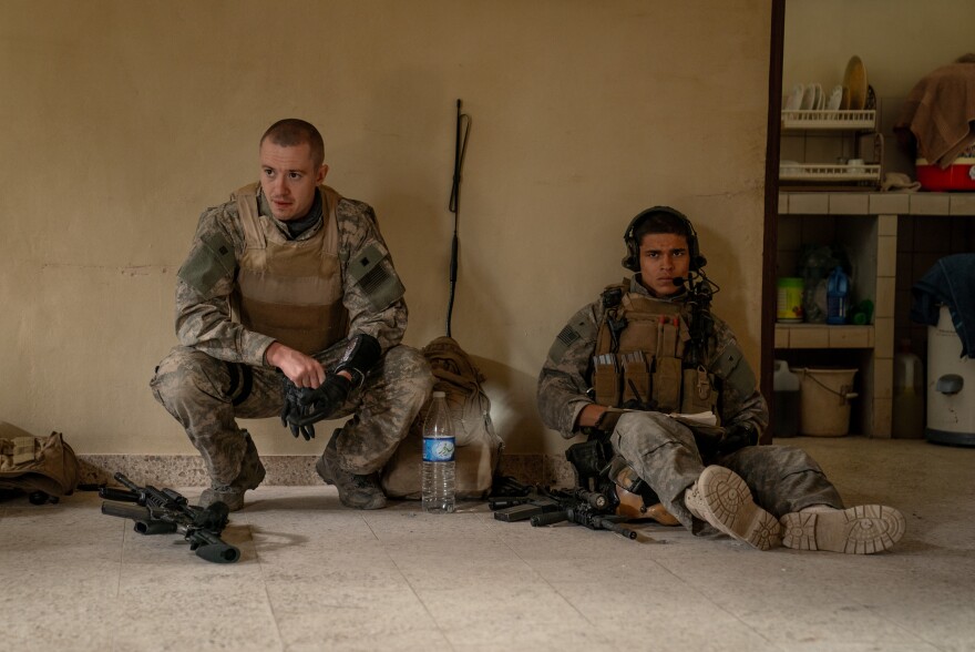Two men sit side by side in army gear. 
