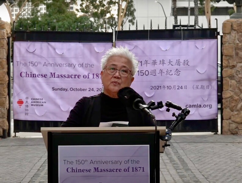 Gay Yuen, a Chinese American woman who heads the Chinese American Museum, speaks in front of a podium set outdoors.