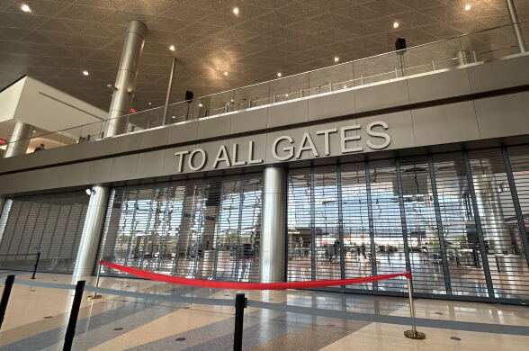 A wide look at the blocked off gate entrance area. It says to all gates in large letters. A red ribbon is across.