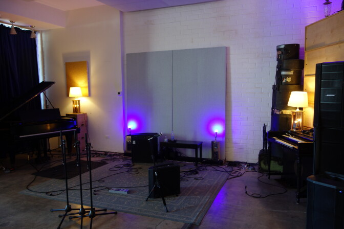 An empty stage with a piano, an organ, an amplifier and several mic stands.