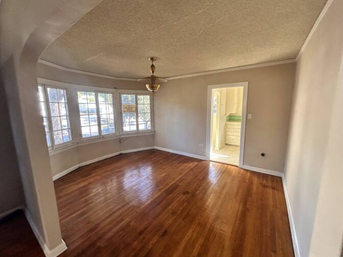 A large, empty dining room area with wooden floors and an open door to the right.