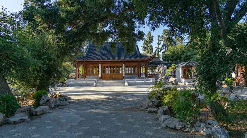 An exterior shot of a brown temple in the Chinese Garden at The Huntington. It's taken from several yards away, frame by green trees in the foreground.