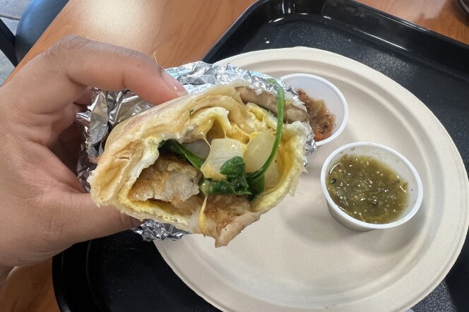 A person holding a half eaten burrito. Salsa verde is visible in a container on a paper plate. 