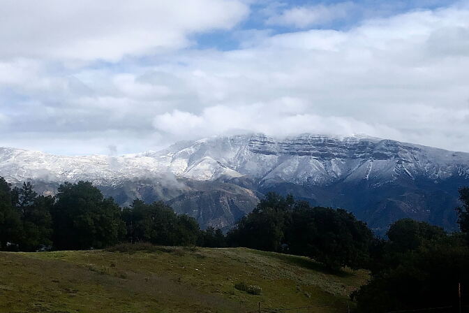 Snow capped mountains rise above a grassy hill 