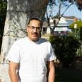 A man stands in front of a tree in a residential neighborhood.